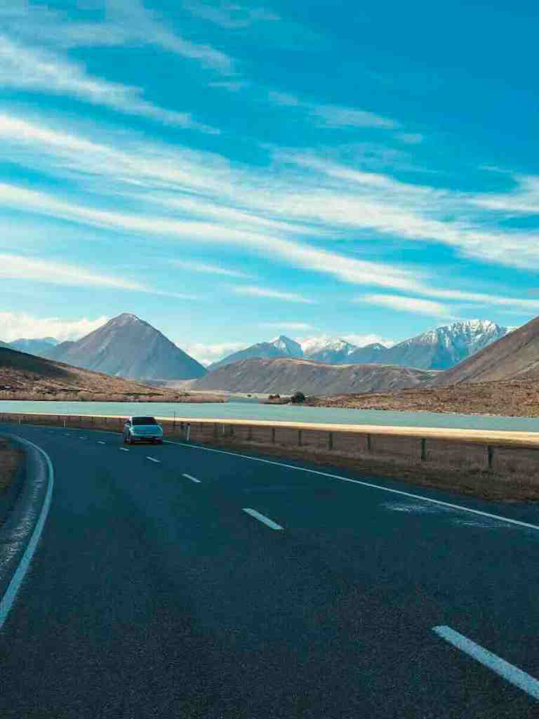 Open South Island highway beneath blue sky with mountains rising in the distance.