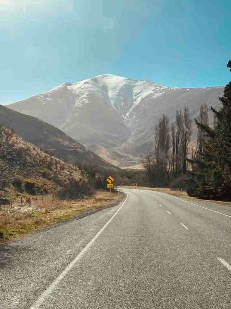 Straight alpine road leading toward a snow-covered mountain near Arthur’s Pass on New Zealand’s South Island.