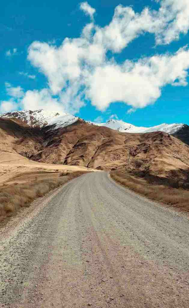 Crown Range Road crossing dry alpine terrain beneath snow-dusted mountains.