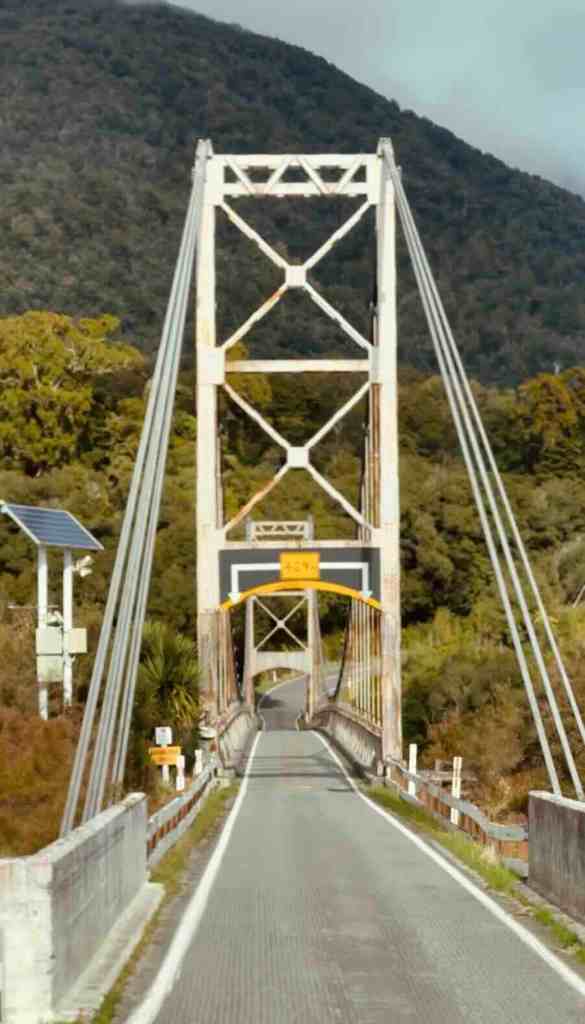 Single-lane bridge on SH6 surrounded by forested mountains along the Haast Pass route.