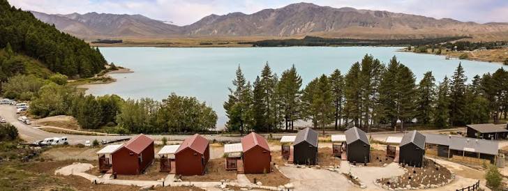 Lakeside holiday park accommodation at Lake Tekapo with cabins, turquoise water and mountains in the distance.
