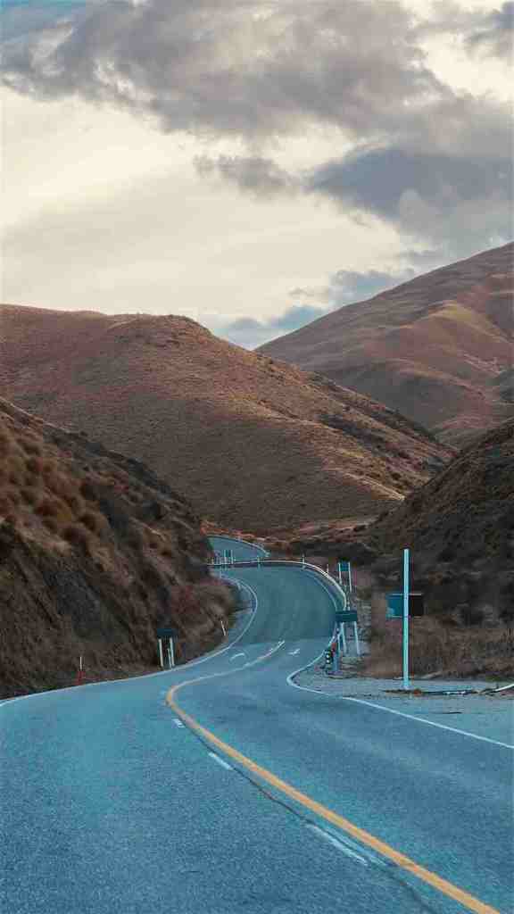 SH6 curving through dry Central Otago mountains beside turquoise water in Kawarau Gorge.