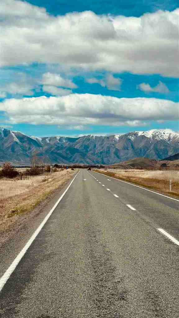 Straight section of SH8 leading toward the mountains of Lindis Pass beneath a blue sky.