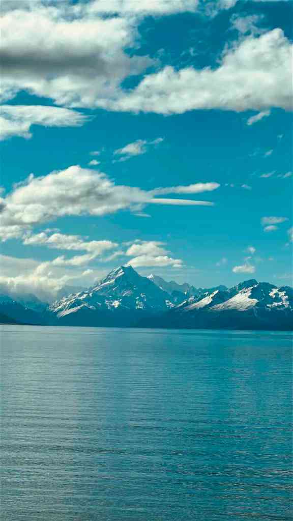 Bright turquoise Lake Pūkaki with snow-covered Southern Alps beneath a blue sky.