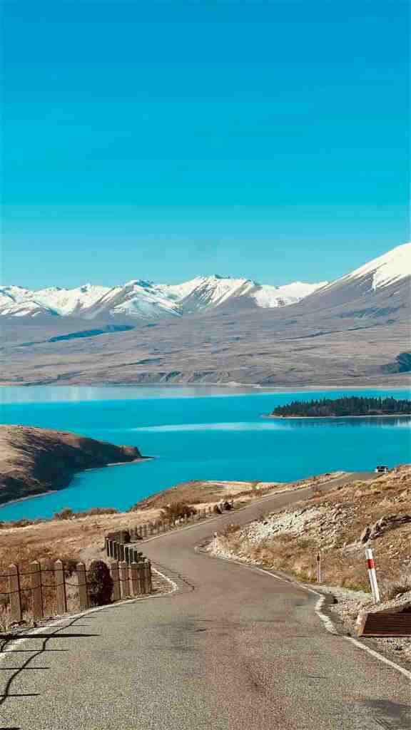 Driving beside a bright turquoise alpine lake and snow-covered mountains on our New Zealand South Island road trip.