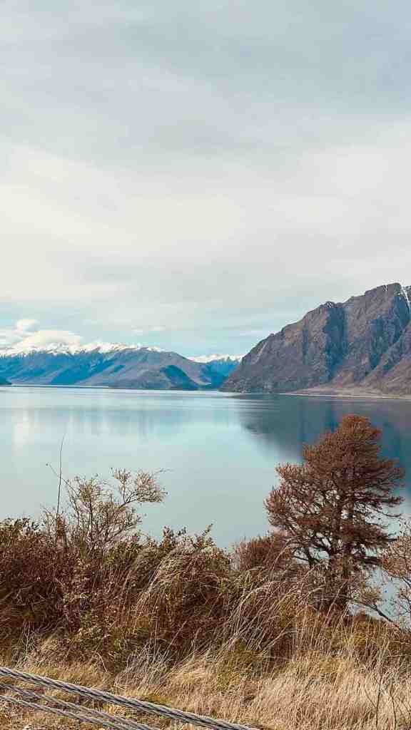 Blue Lake Hāwea surrounded by steep mountains beside the South Island highway.