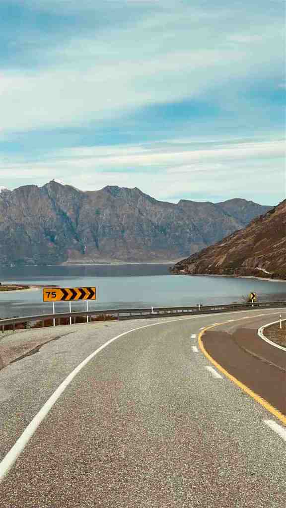 Curving road beside Lake Hāwea and steep mountains near The Neck.