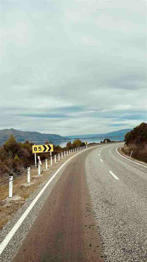 SH6 running beside Lake Hāwea with mountain scenery ahead.