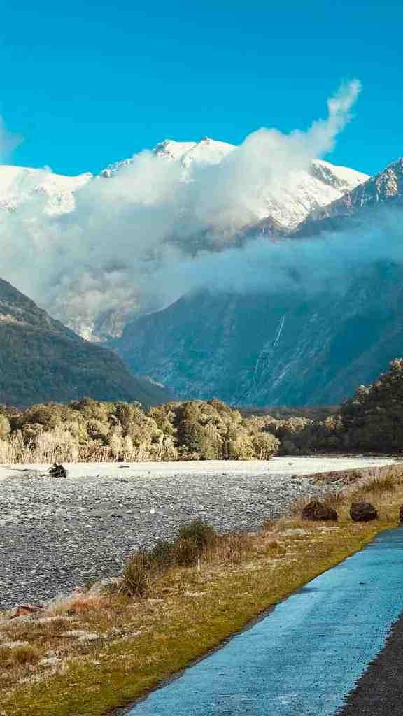 West Coast mountain valley with cloud-covered peaks rising above a wide riverbed beside SH6.